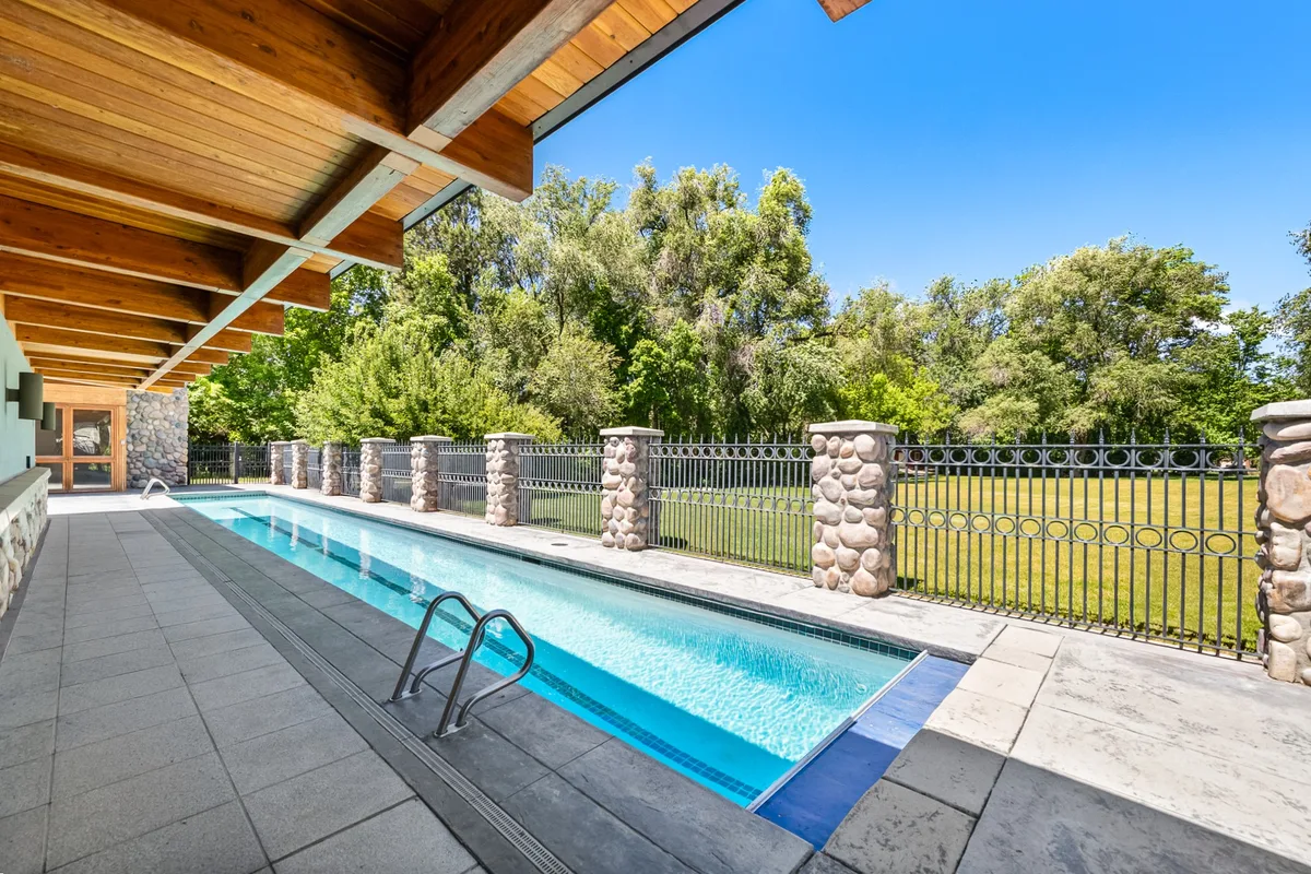 Lap pool framed by stonework, trees, and blue sky